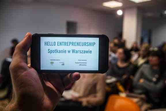 In the foreground a phone with text: Hello Entrepreneurship, in the background a room full of people