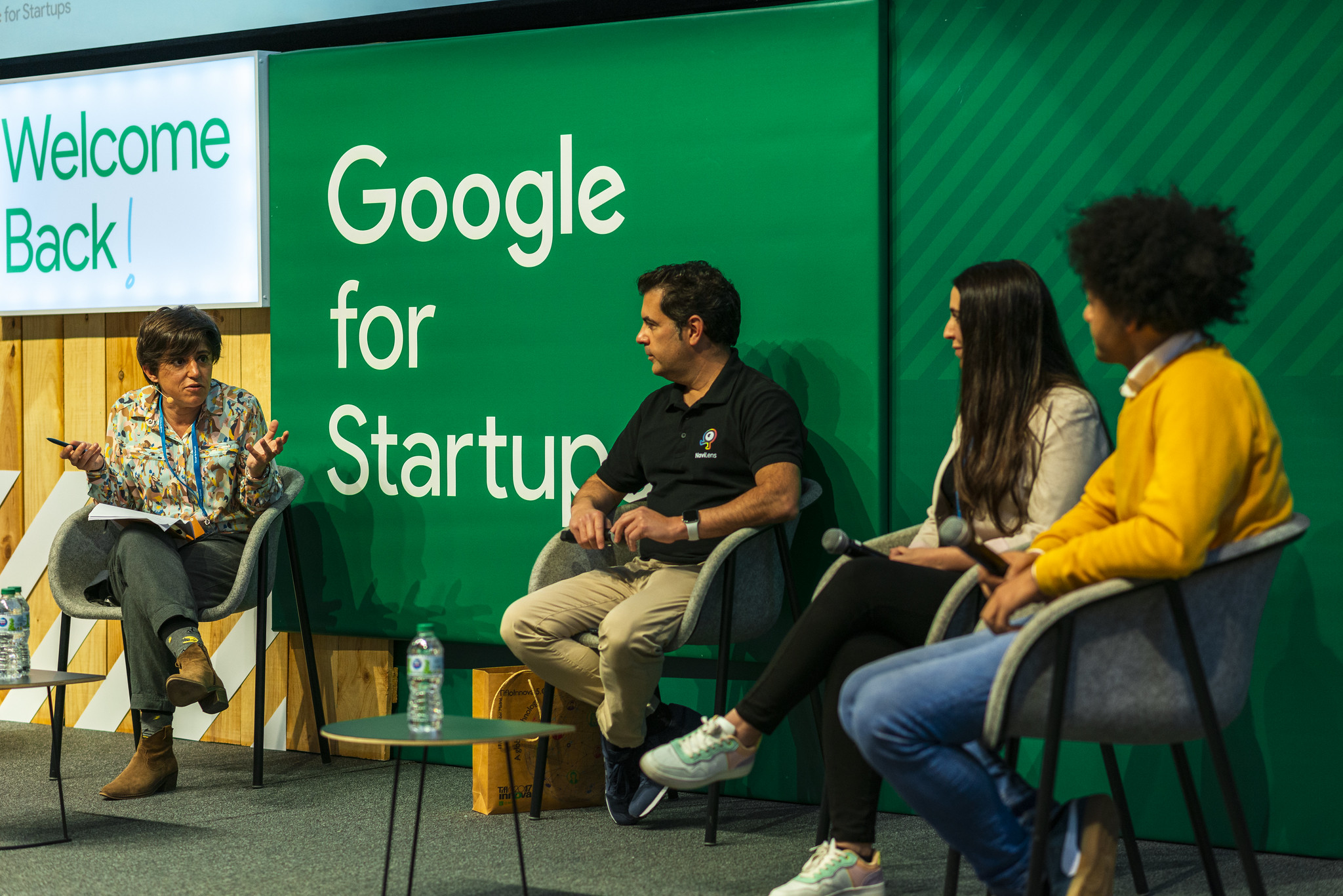 Group of people on a stage in panel format talking. Background a green wall that says "Google for Startup"