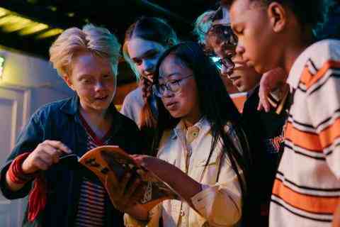 The photo shows are multicultural group of children who are all looking at a book held by one of the girls.