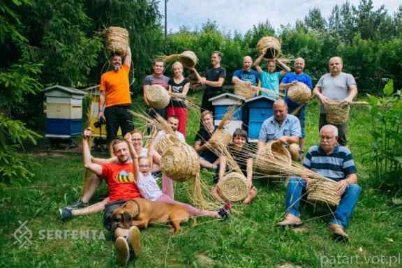 Grupa osób pozuje do zdjęcia na trawie. W dłoniach trzymają własnoręcznie uplecione koszyki.