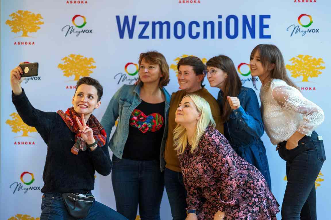 Na tle ścianki zdjęciowej z napisem Wzmocnione oraz logo Ashoki i Magovox 6 kobiet robi sobie selfie.