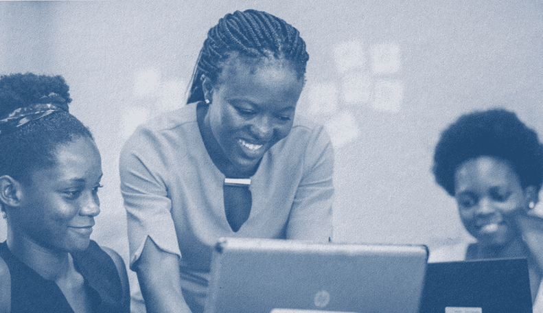 Photo shaded in dark blue. Three people huddle over a few laptops, smiling and looking at the laptops, as if they are working on something together