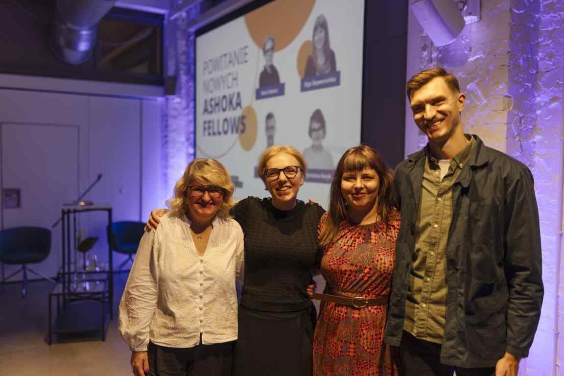 Zdjęcie przedstawia 4 Ashoka Fellows na spotkaniu witającym ich w społeczności Ashoki. Od lewej Myroslava Keryk, Maria Deskur, Olga Ślepowrońska i Maciej Otrębski. W tle widać filetowe światła i rzutnik.