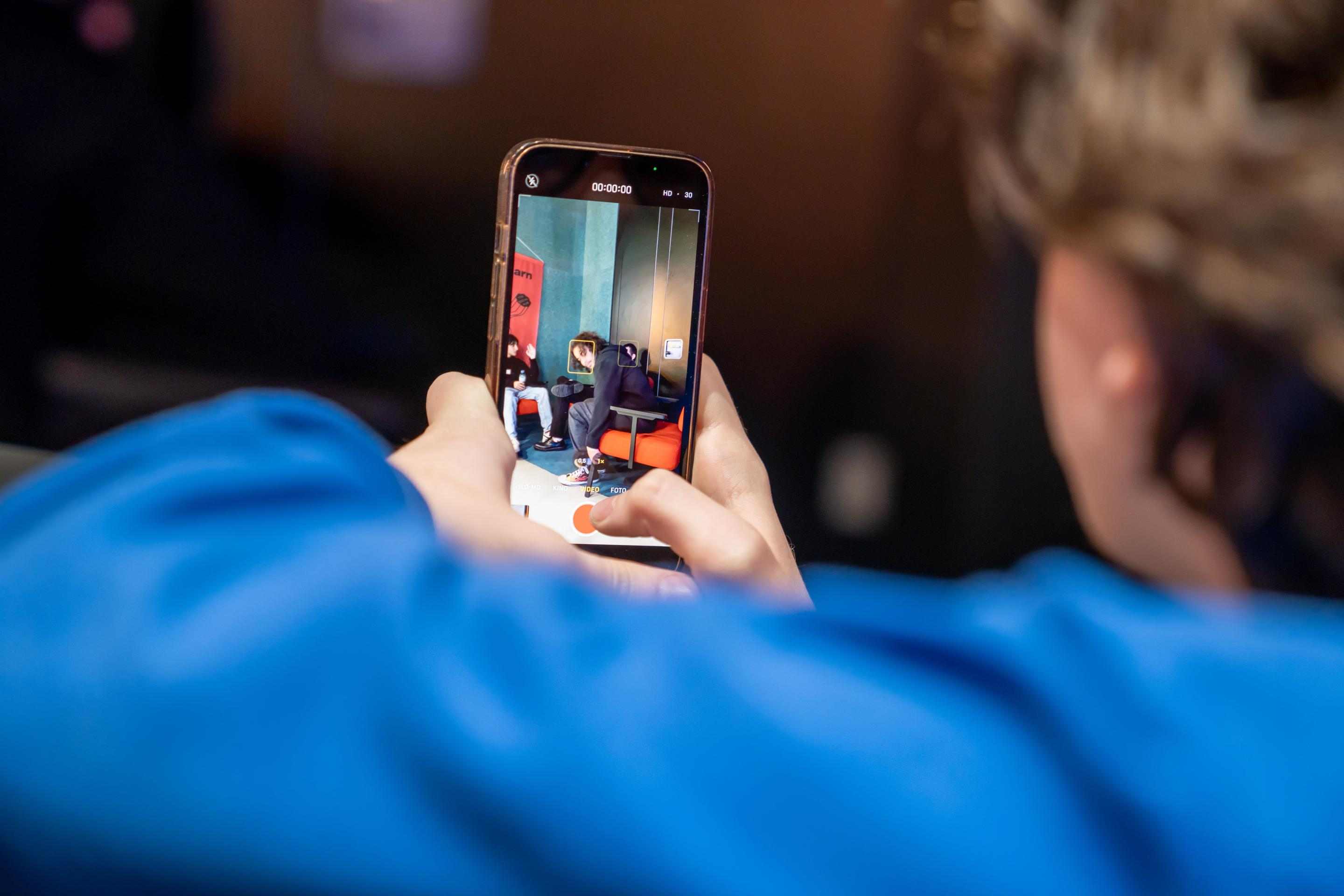 Photo from behind of boy filming with the smartphone