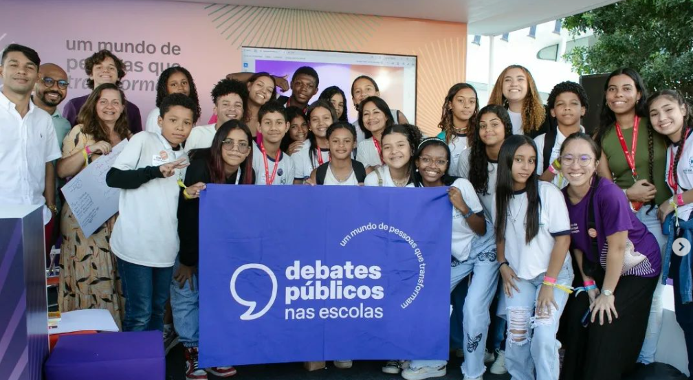 Um grupo de jovens reunidos segurando a bandeira dos Debates Públicos das Escolas