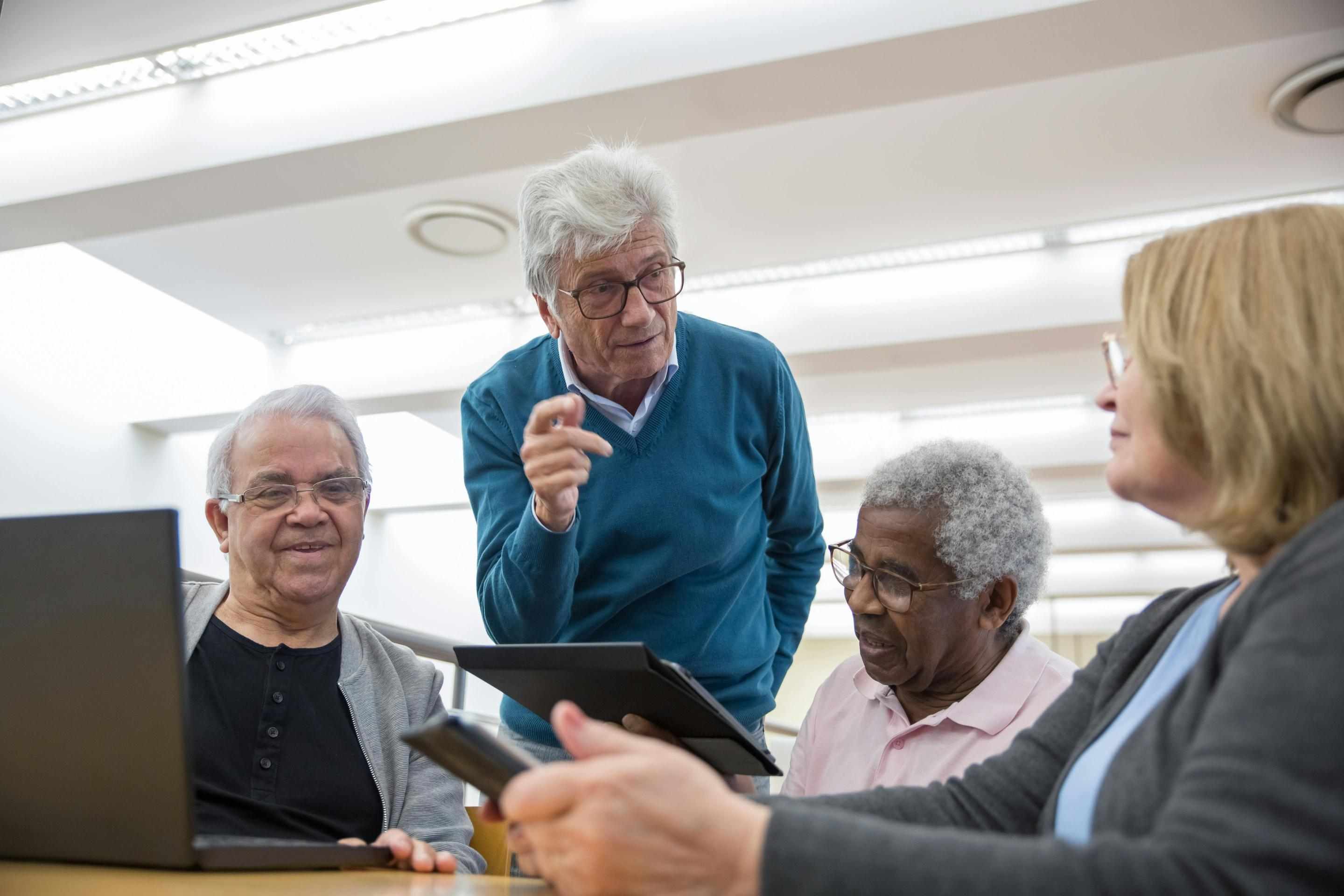 Fotografía de cuatro personas mayores hablando sobre dispositivos electrónicos