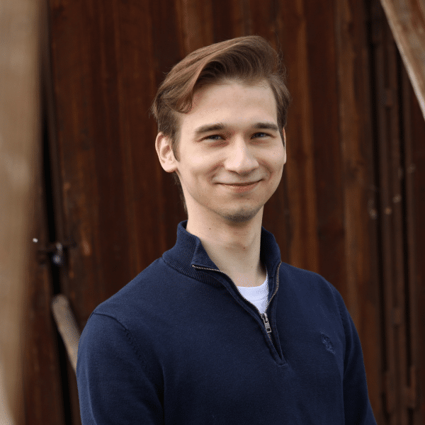 Young man standing in front of wooden wall, smiling