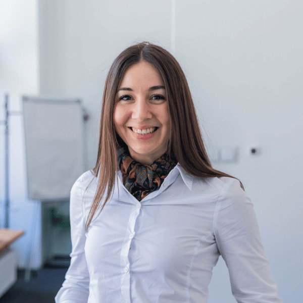 Young woman with long hair wearing white shirt, standing in a conference room, smiling