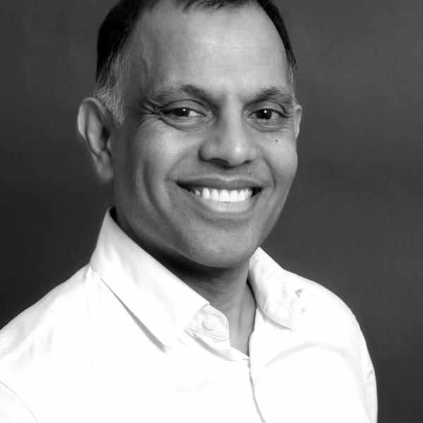 Person with short hair and a white collared shirt smiling at the camera slight profile left. Background is a black wall