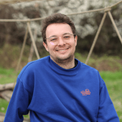 Young man with a glasses in a blue hoodie sitting outside, smiling