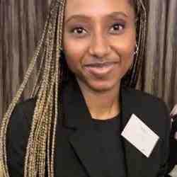 Photo of Mtha Nazo, staff member with Ashoka Africa. Person with long blonde braids and darker skin smiling at the camera, dressed in a professional black long sleeved shirt with a long collar