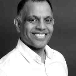 Person with short hair and a white collared shirt smiling at the camera slight profile left. Background is a black wall