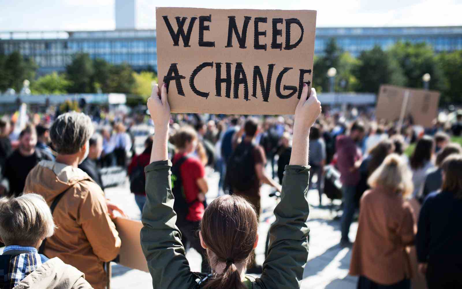 Young person at a rally of climate activist holding a sign that says "We need a change"