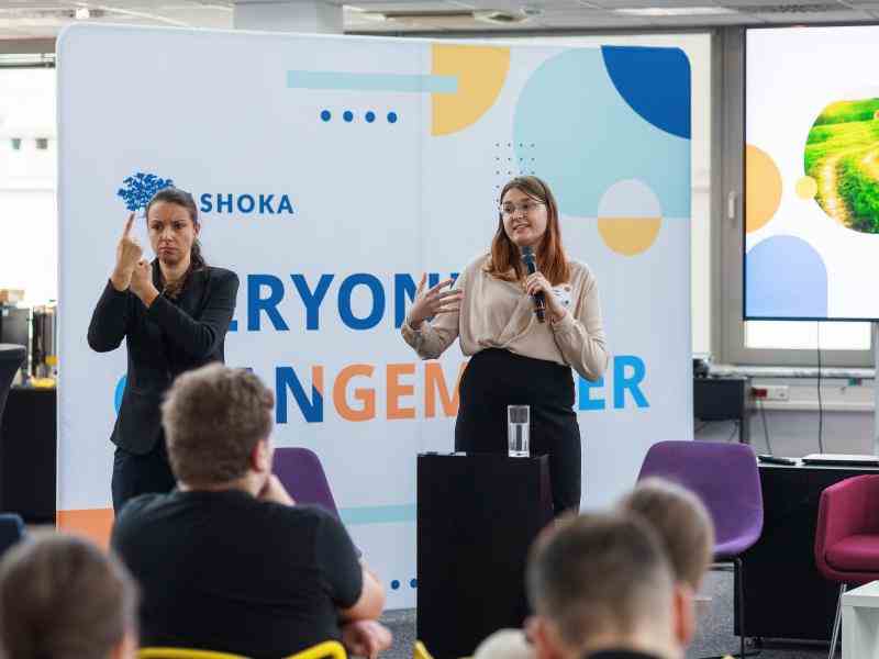 A woman speaking on stage, next to her another woman translating to sign language